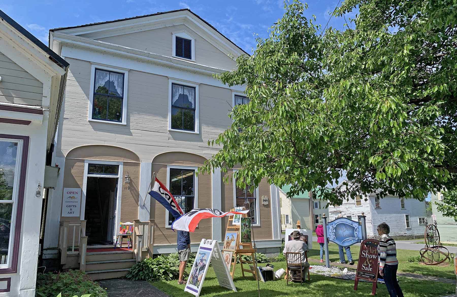 Photo of the Samuel F. Hooker House on a sunny day in 2022, taken by Kathy Keating. Since its restoration by the Sackets Harbor Historical Society, the building has been used as the gallery for the Arts Association of Northern New York (AANNY)
